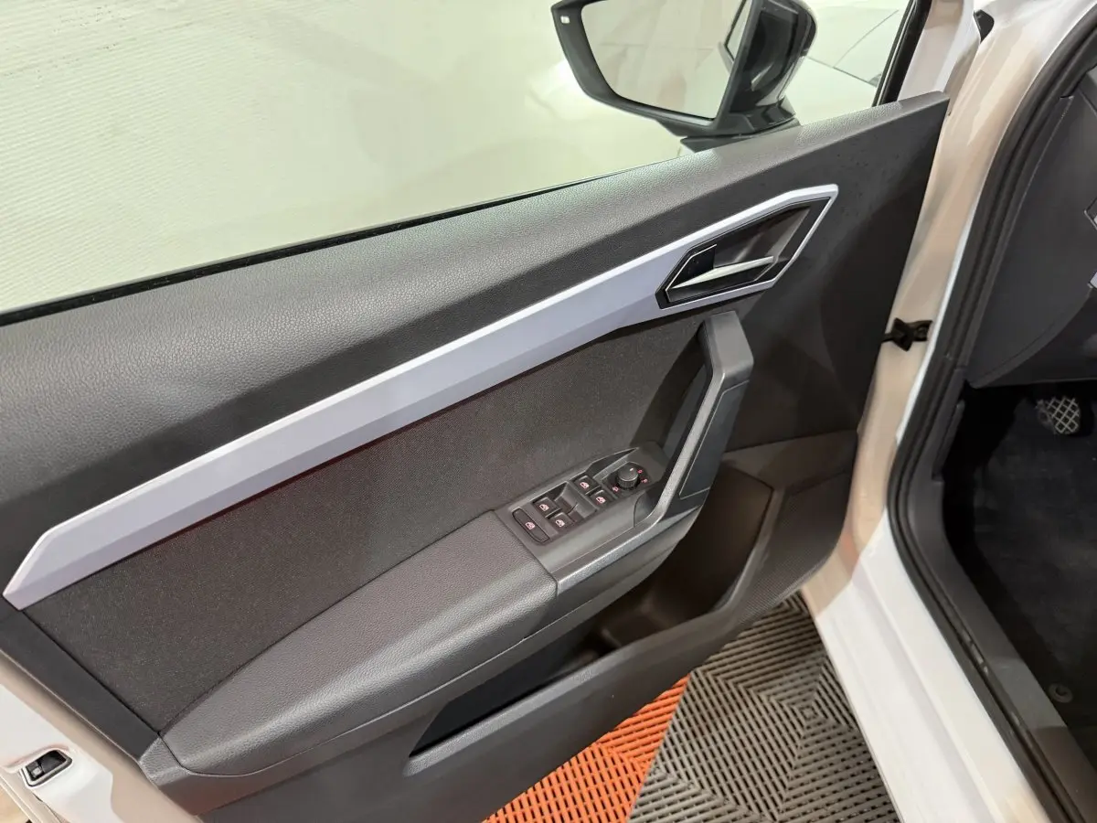 Vue intérieure côté gauche de la porte avant blanche d'une SEAT Ibiza 2024 avec commandes électriques et poignée angulaire.