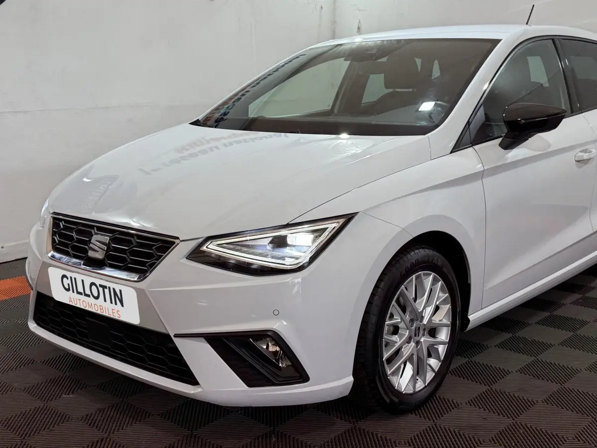 Vue 3/4 avant droit d'une SEAT Ibiza blanche avec phares LED et jantes alliage multibranches.