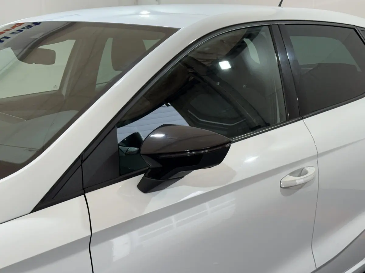 Vue latérale gauche rapprochée d'une SEAT Ibiza blanche 2024 avec rétroviseur noir brillant et poignée de porte intégrée.