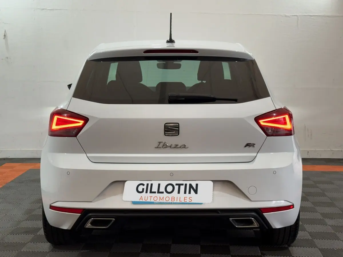 Vue arrière d'une SEAT Ibiza 1.0 TSI 110 FR blanche avec feux LED triangulaires allumés en intérieur.