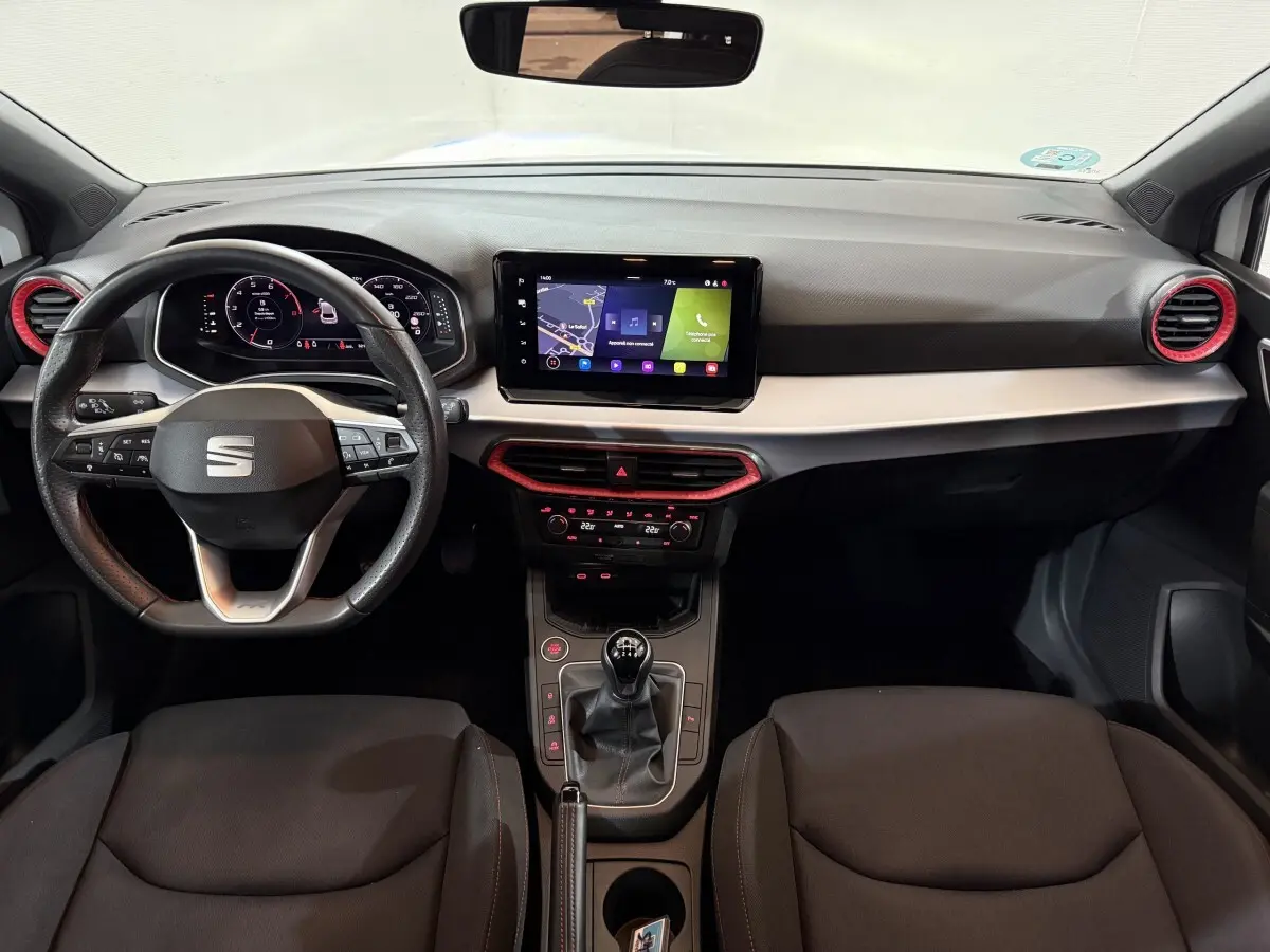 Vue intérieure avant du tableau de bord de la SEAT Ibiza 1.0 TSI 110 FR avec volant cuir, écran tactile et détails rouges.