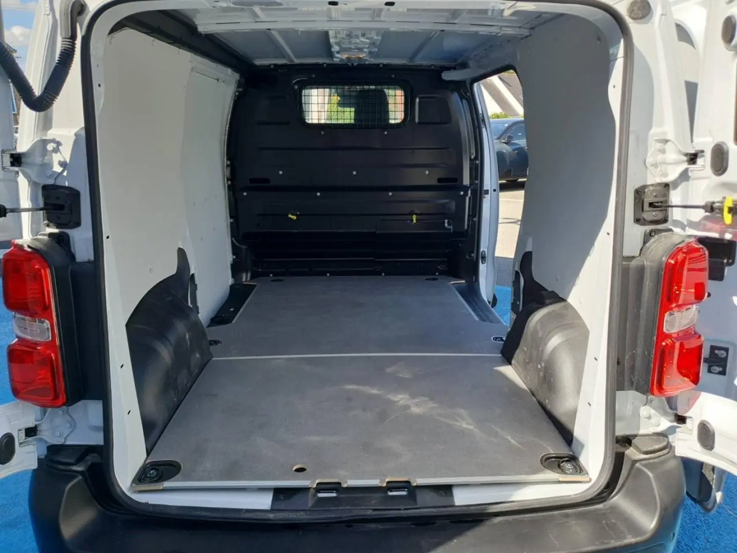 Vue arrière ouverte du Toyota Proace Fourgon blanc Glacier, montrant l'espace de chargement vide avec plancher bois et cloison pleine noire.