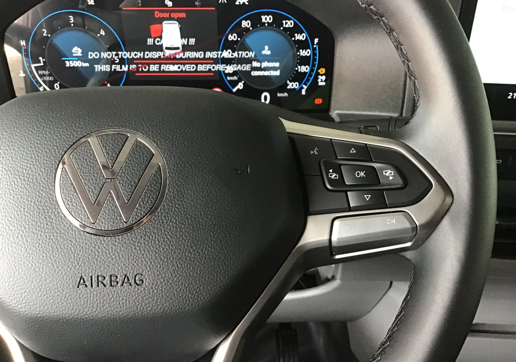 Gros plan sur le volant noir du Volkswagen Transporter T7 avec commandes intégrées et tableau de bord digital en arrière-plan.