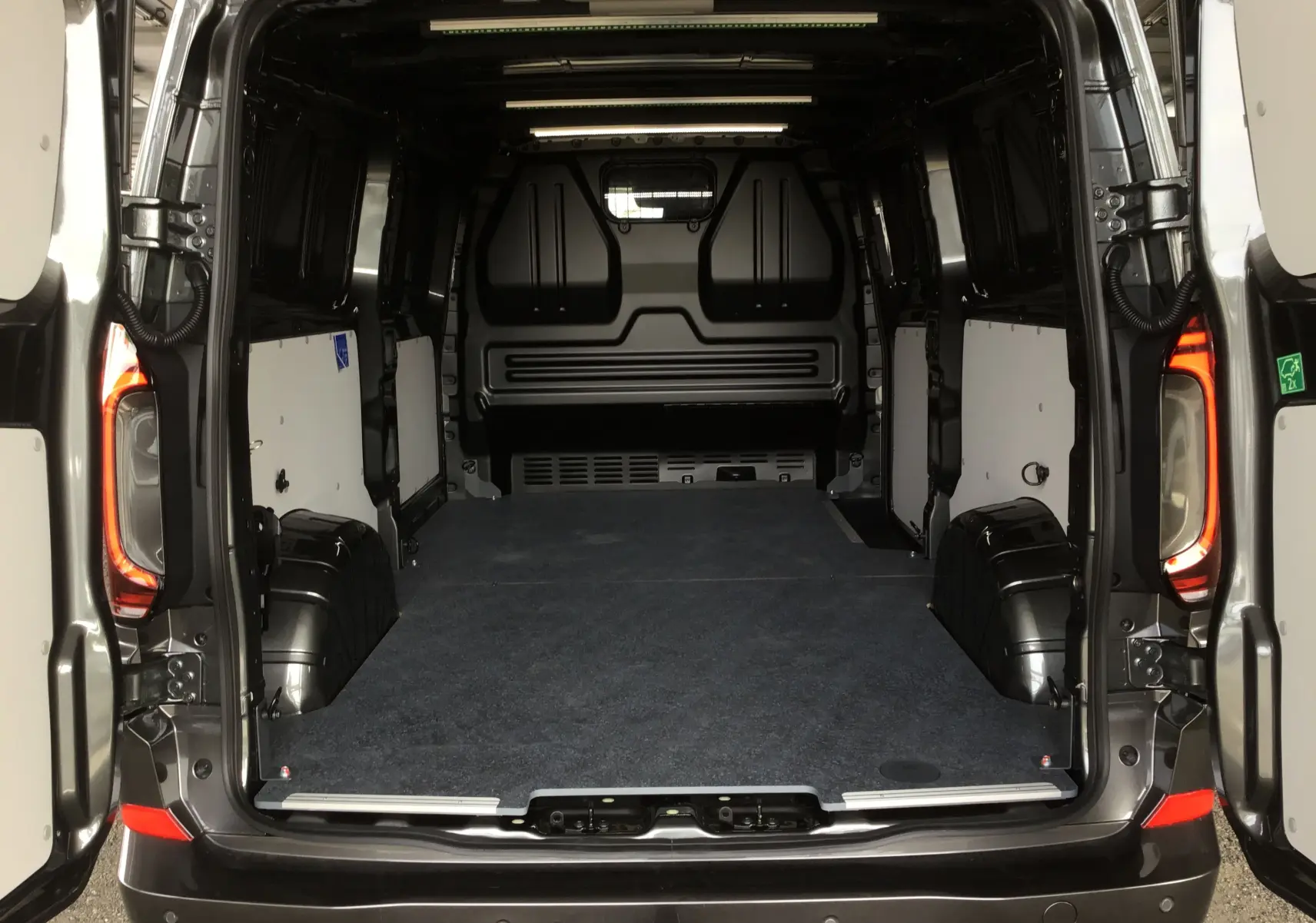 Vue arrière du Volkswagen Transporter T7 gris anthracite avec portes ouvertes montrant l'espace de chargement vide et aménagé.