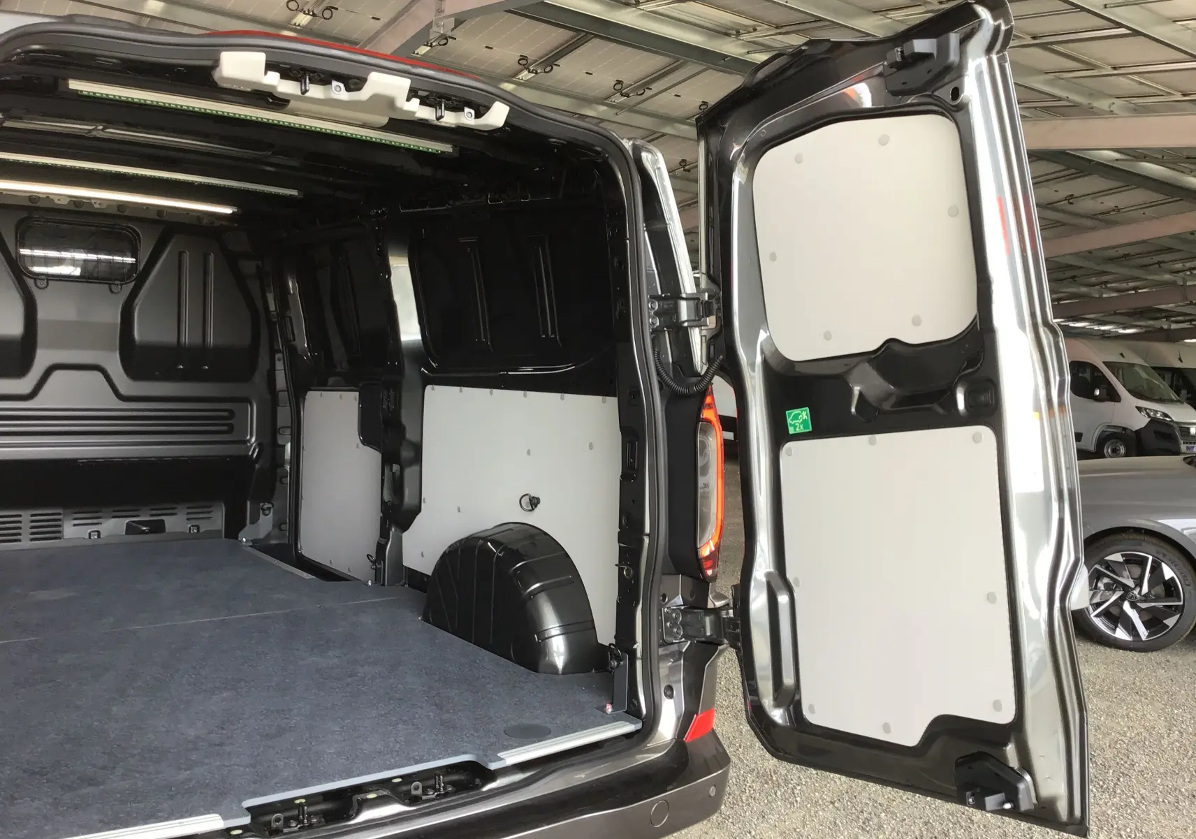 Vue arrière ouverte du Volkswagen Transporter T7 gris anthracite, montrant l'espace de chargement et la porte battante droite.