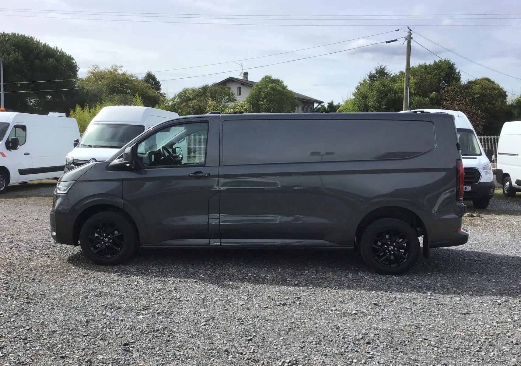 Vue de profil côté gauche d'un Volkswagen Transporter T7 gris anthracite avec jantes noires et barres de toit repliables.