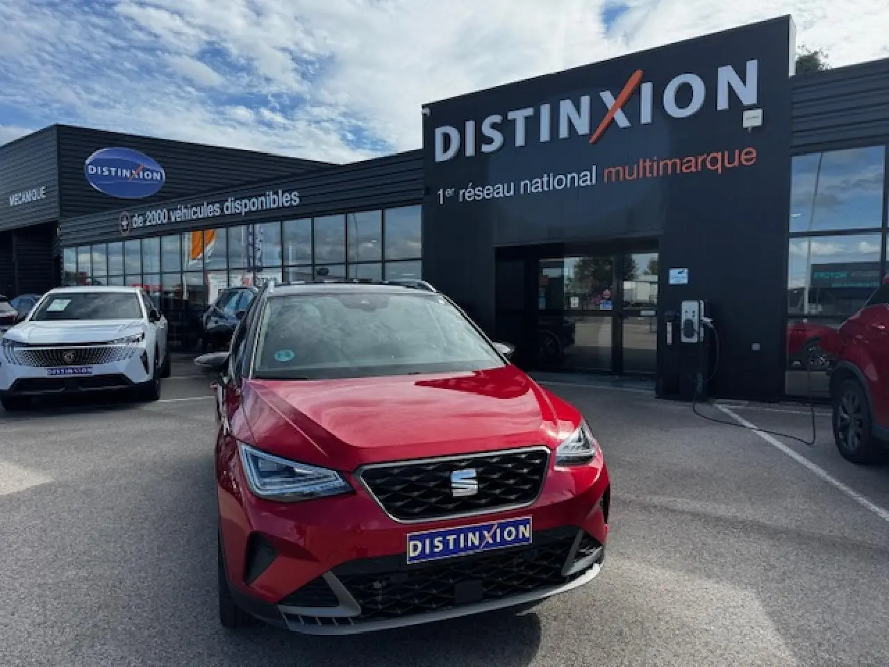 Vue avant d'une SEAT Arona rouge Désir avec toit noir, calandre FR et phares Full LED, devant un concessionnaire Distinxion.