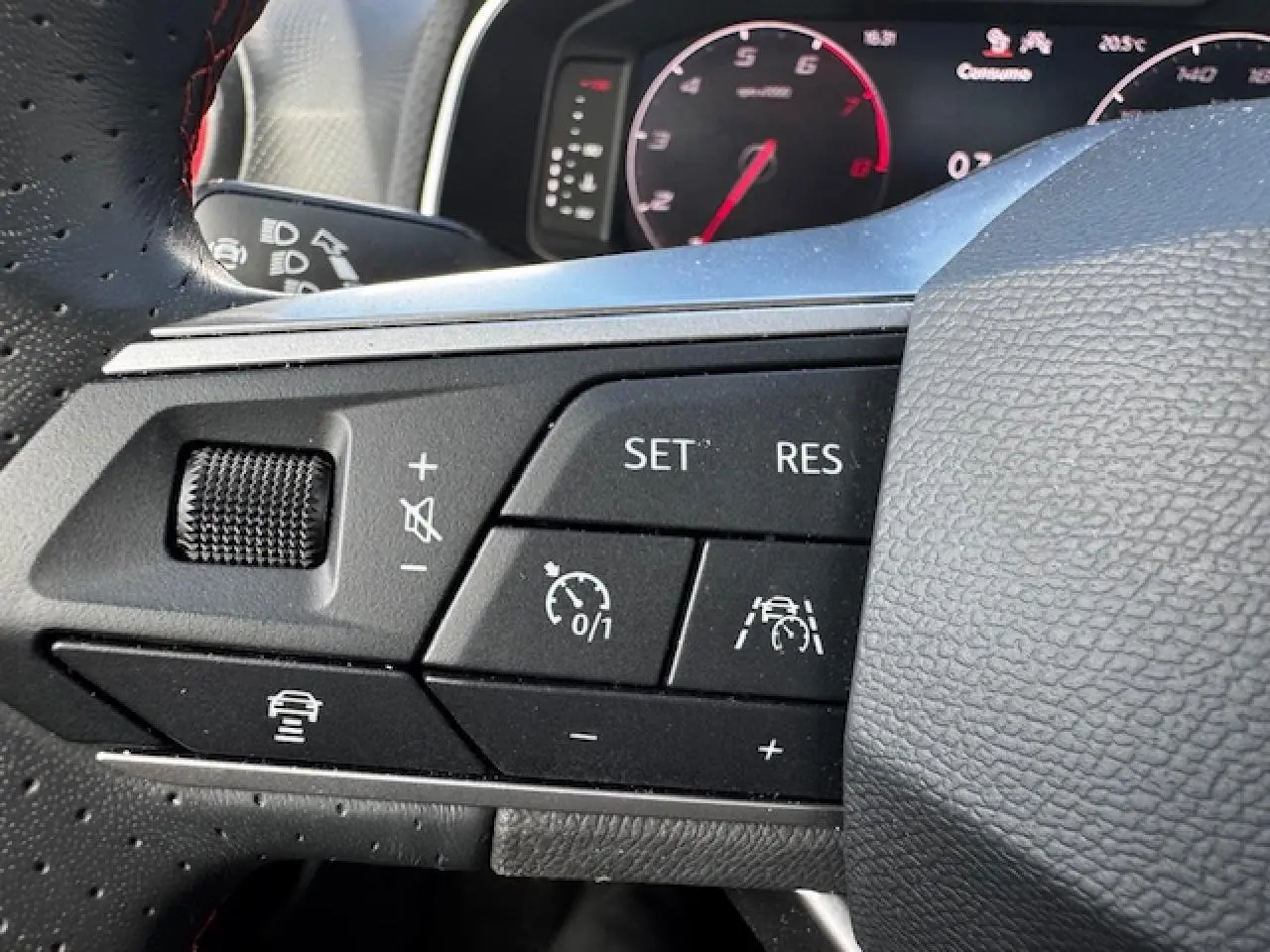 Gros plan sur les commandes du volant côté gauche du SEAT Arona 2024 avec surpiqûres rouges et fonctions d’aide à la conduite.