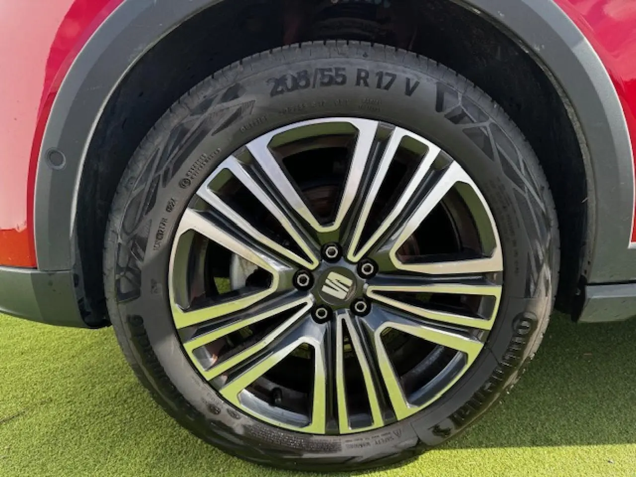 Gros plan sur la jante alliage 17 pouces du SEAT Arona rouge Désir avec logo central sur fond d'herbe verte.