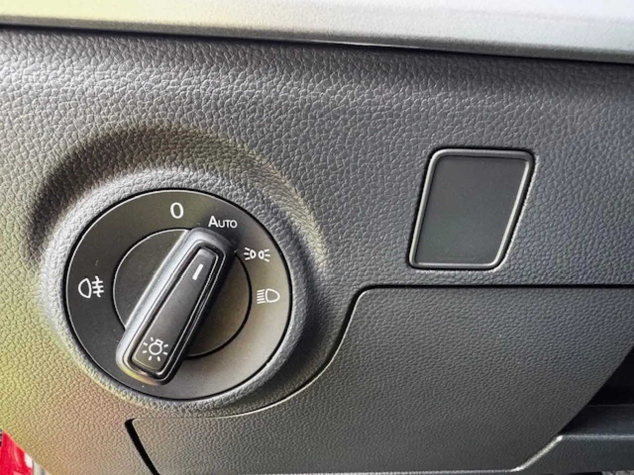 Gros plan sur le bouton de commande des phares dans l'habitacle du SEAT Arona 2024 rouge Désir avec toit noir.