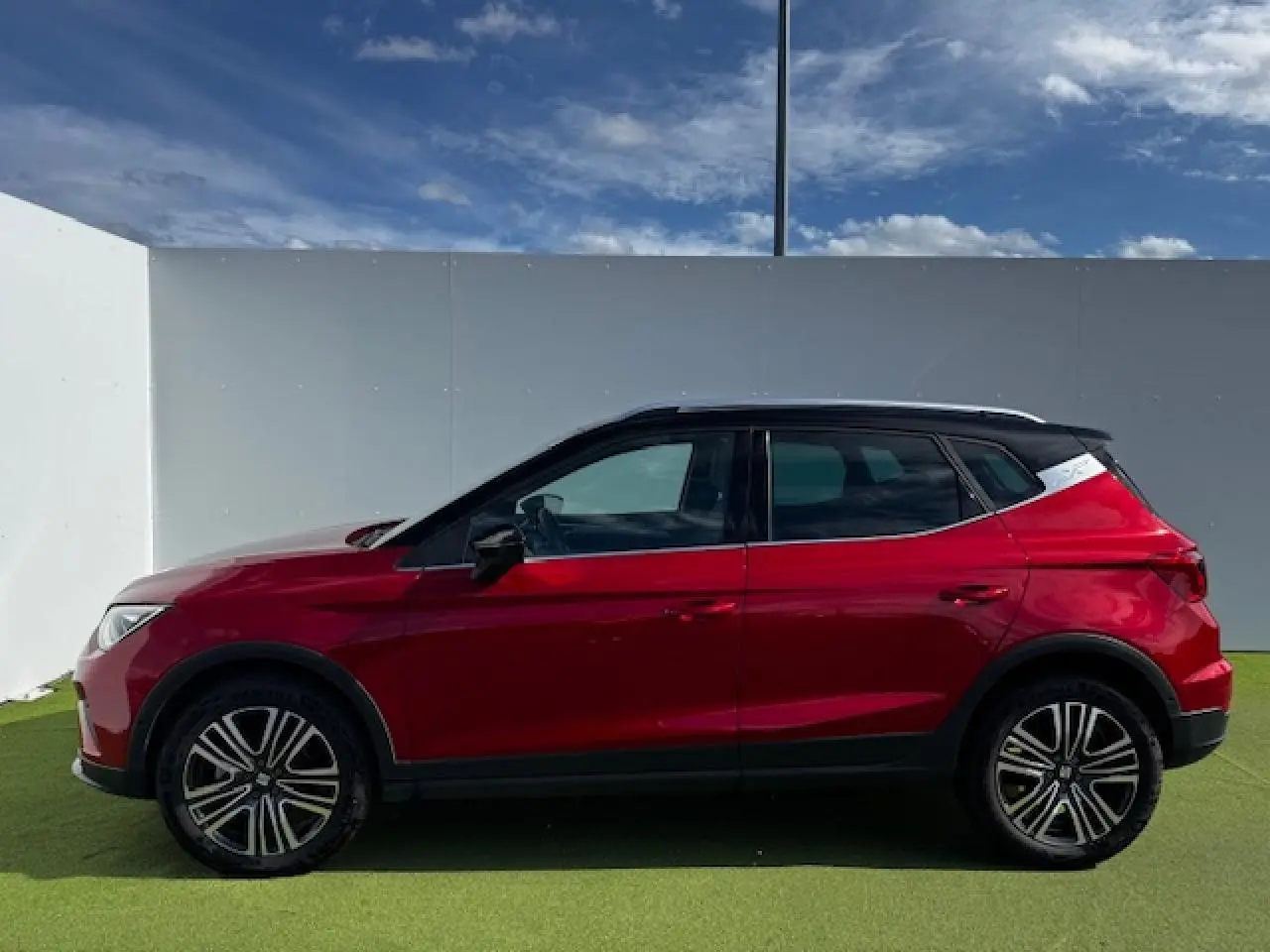 Vue latérale droite d'un SEAT Arona 2024 rouge Désir avec toit noir et jantes alliage noires.