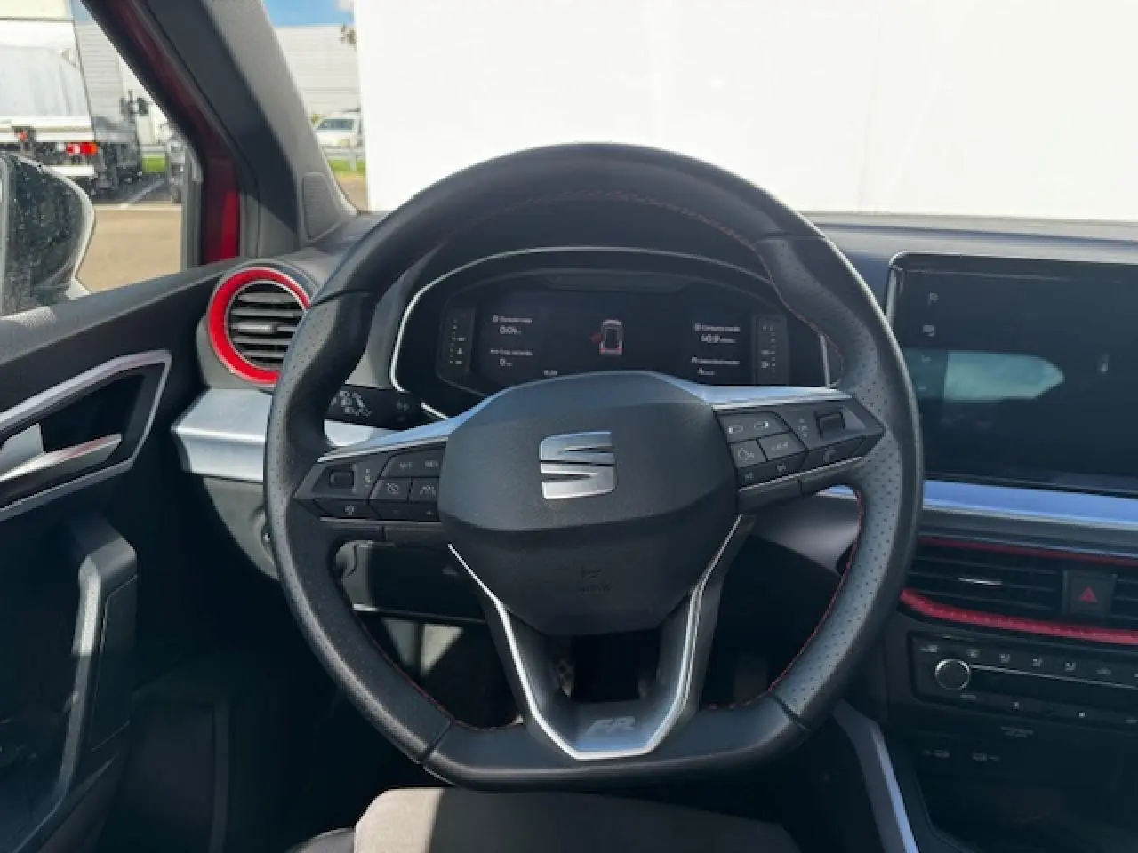 Vue intérieure centrée sur le volant sport en cuir perforé avec surpiqûres rouges du SEAT Arona FR 2024.