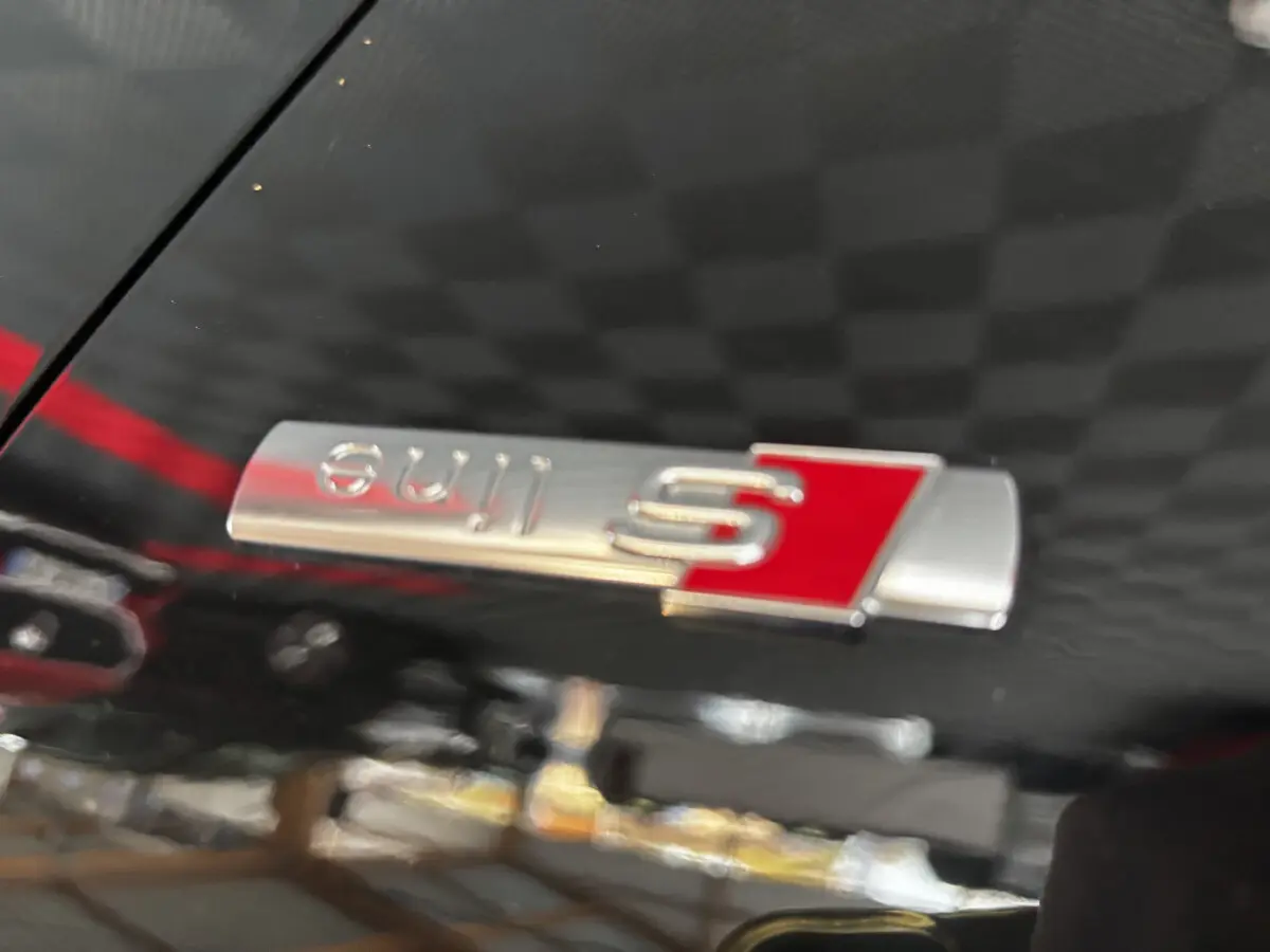 Gros plan sur l’emblème S line argent et rouge sur la carrosserie noire brillante d’un Audi Q2 35 TFSI 2023.