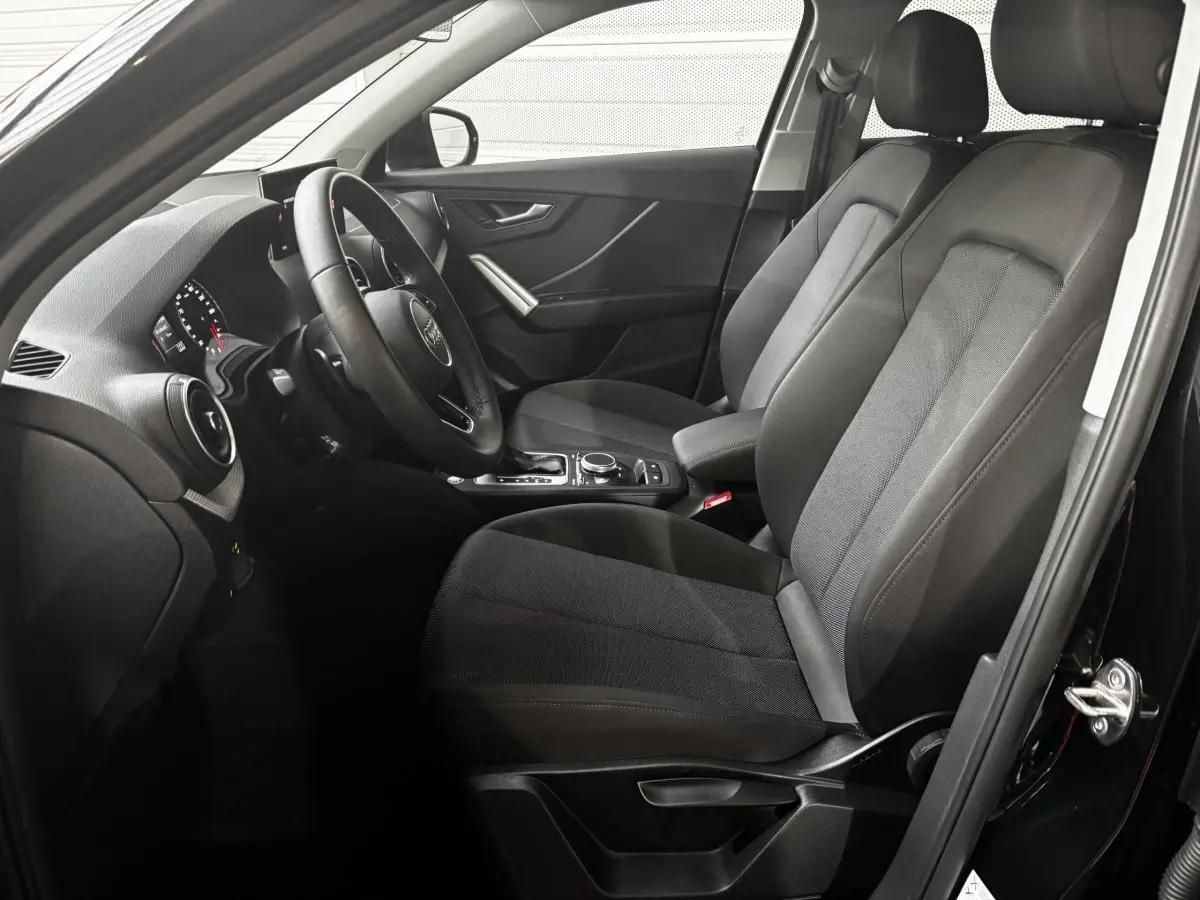 Vue intérieure côté conducteur de l'Audi Q2 noir 2023, mettant en valeur les sièges avant et le volant cuir multifonctions.