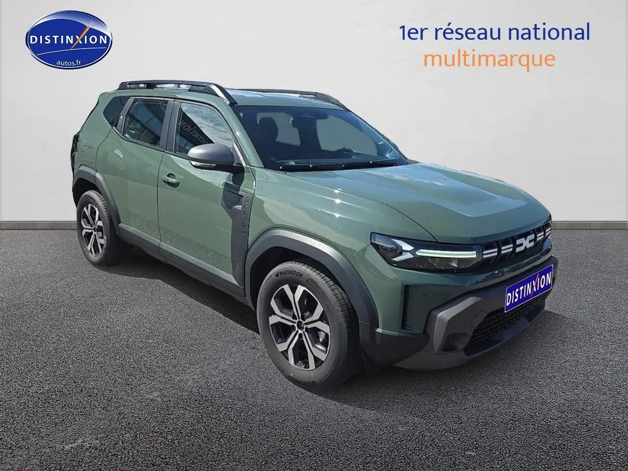 Vue 3/4 avant gauche d'un Dacia Duster 2025 vert kaki avec jantes alu et barres de toit noires.