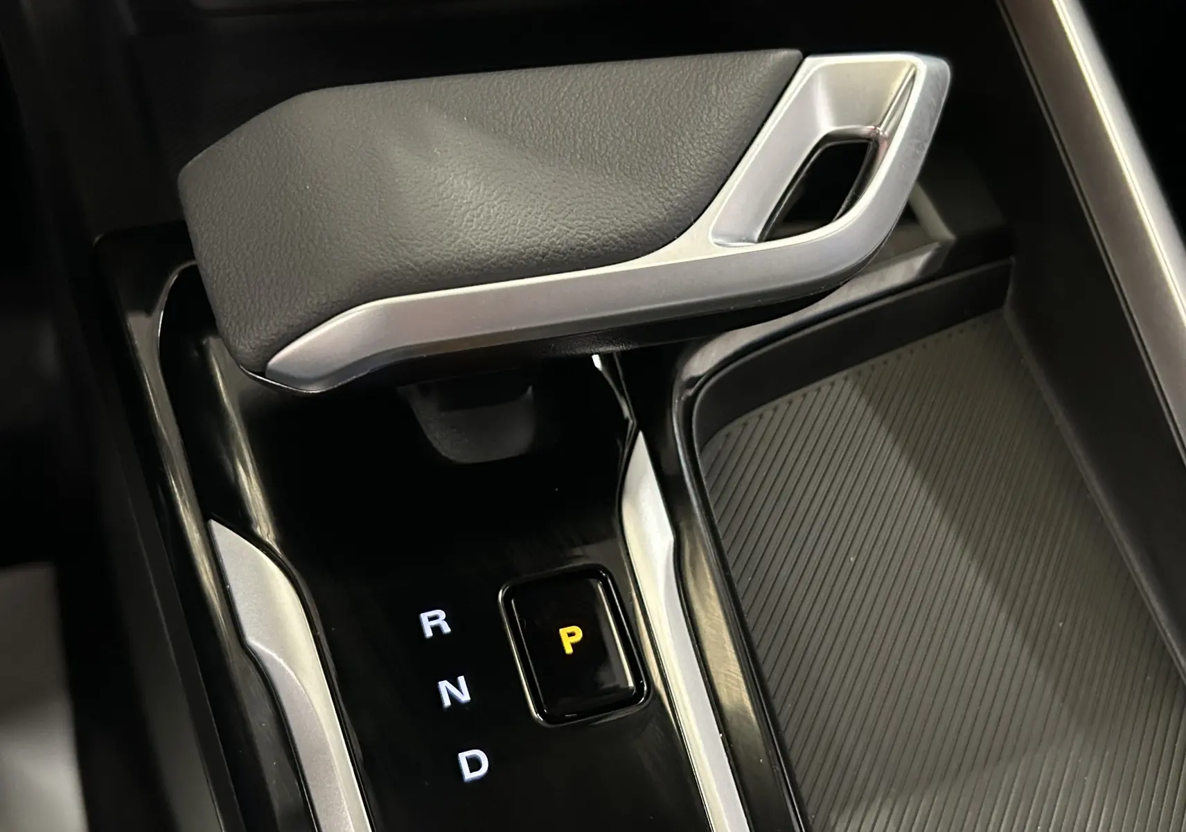Gros plan sur la commande de boîte automatique noire avec levier et indicateur de position P éclairé dans un MG ZS Hybrid+ gris.