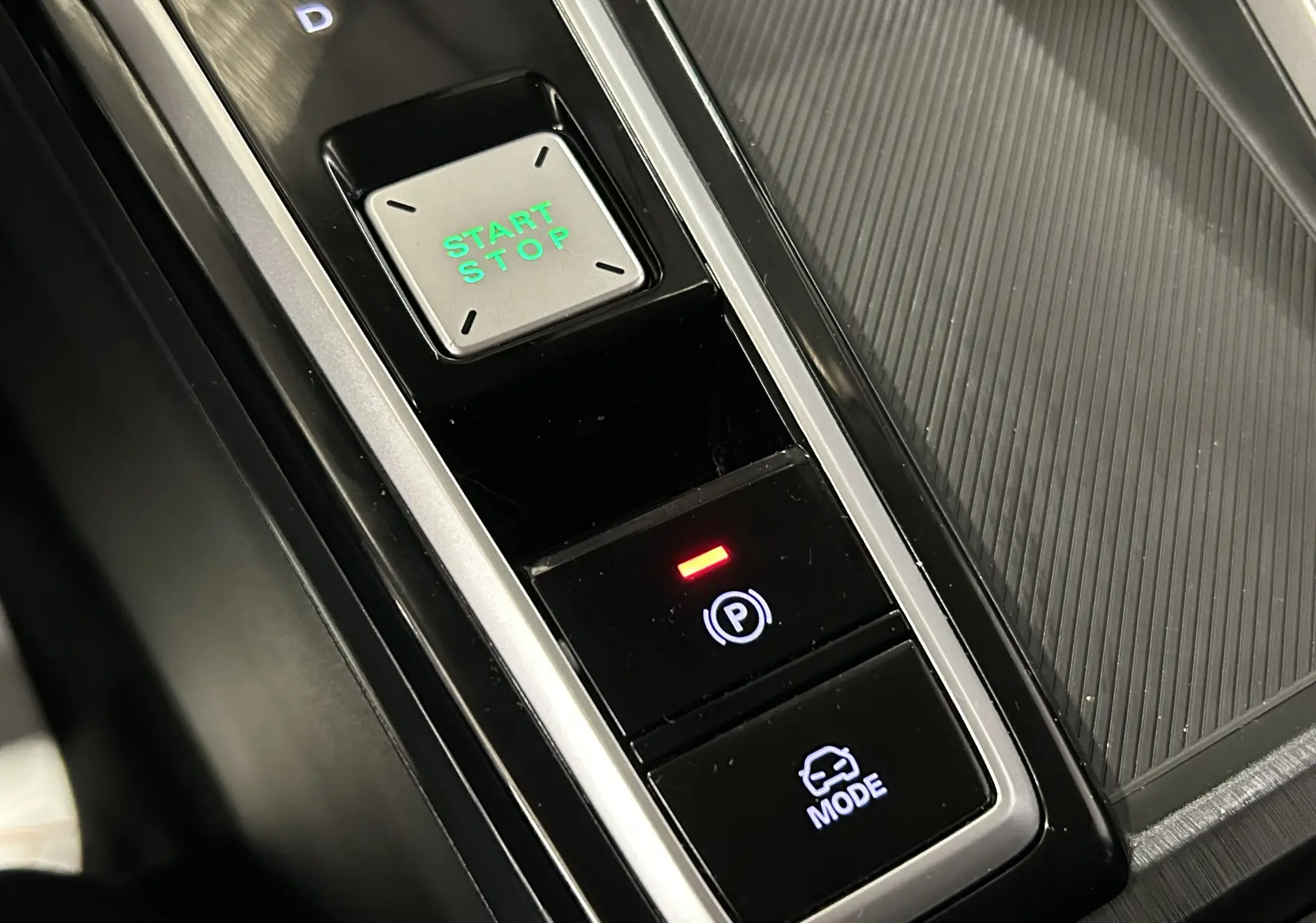 Gros plan sur la console centrale du MG ZS Hybrid+ 2025, avec bouton Start/Stop vert et commandes électroniques noires.