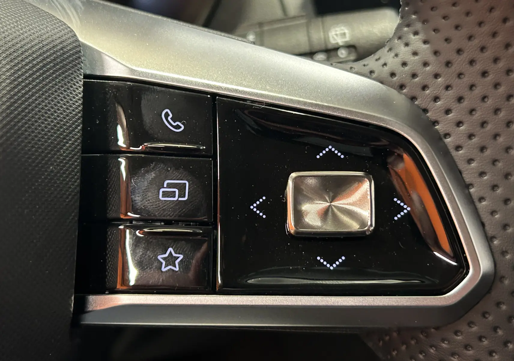 Gros plan sur les commandes multifonctions en plastique noir et métal du volant perforé du MG ZS Hybrid+ 2025.