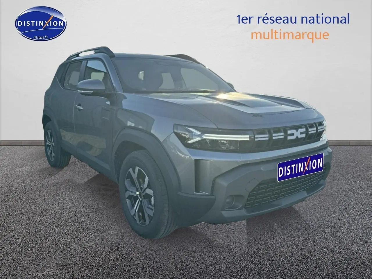 SUV Dacia Duster gris schiste en 3/4 avant droit avec jantes alu et barres de toit visibles.