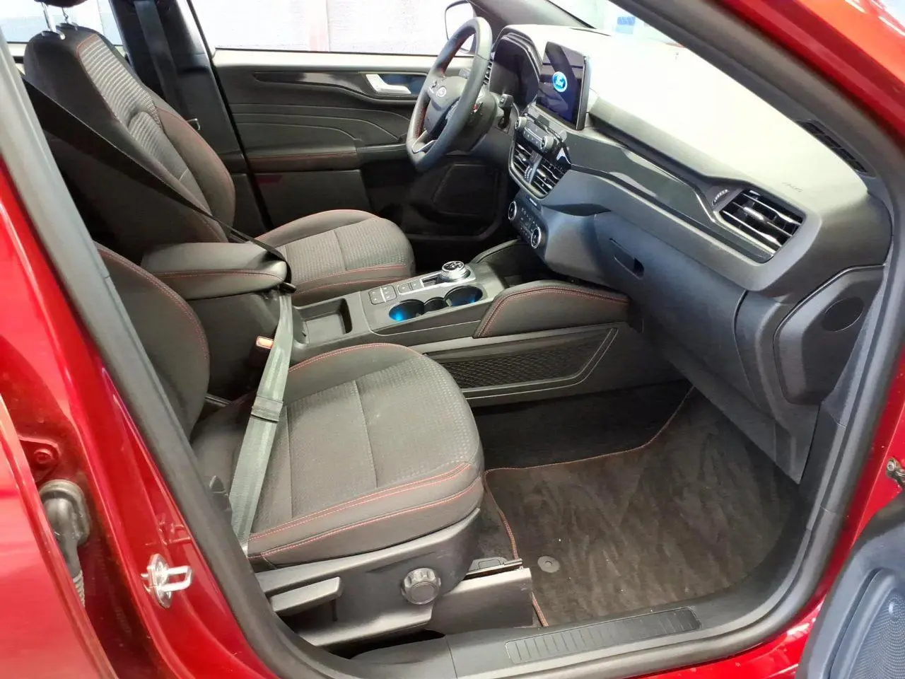 Vue intérieure côté conducteur du Ford Kuga rouge Lucifer 2024, avec sièges noirs et surpiqûres rouges, tableau de bord moderne.
