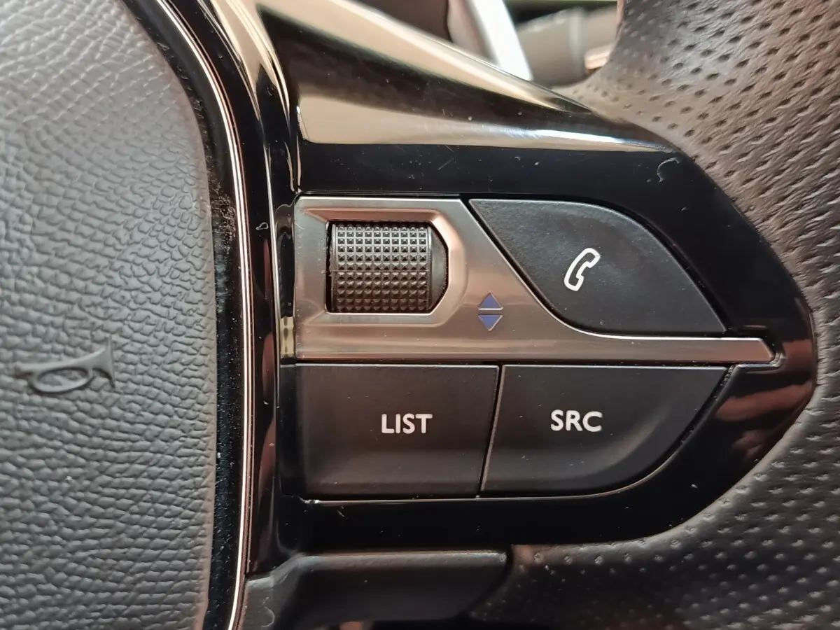 Gros plan sur les commandes gauche du volant cuir perforé du Peugeot 3008 bleu hybride rechargeable.