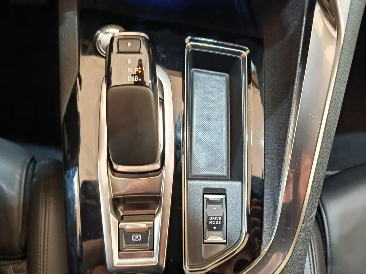 Gros plan sur la console centrale noire brillante du Peugeot 3008 bleu, avec levier de vitesses automatique et bouton Drive Mode.