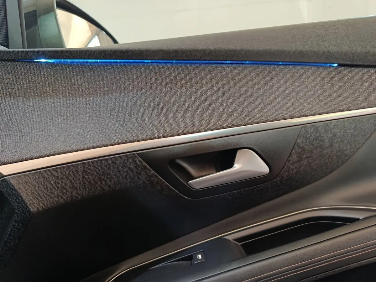 Détail de la porte intérieure côté gauche du Peugeot 3008 bleu, avec éclairage d'ambiance bleu et poignée argentée.