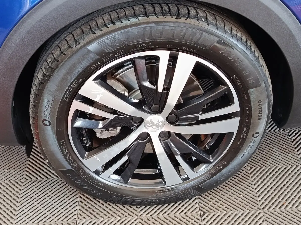 Gros plan sur la roue avant droite du Peugeot 3008 bleu, mettant en valeur la jante alliage bicolore et le pneu Michelin.