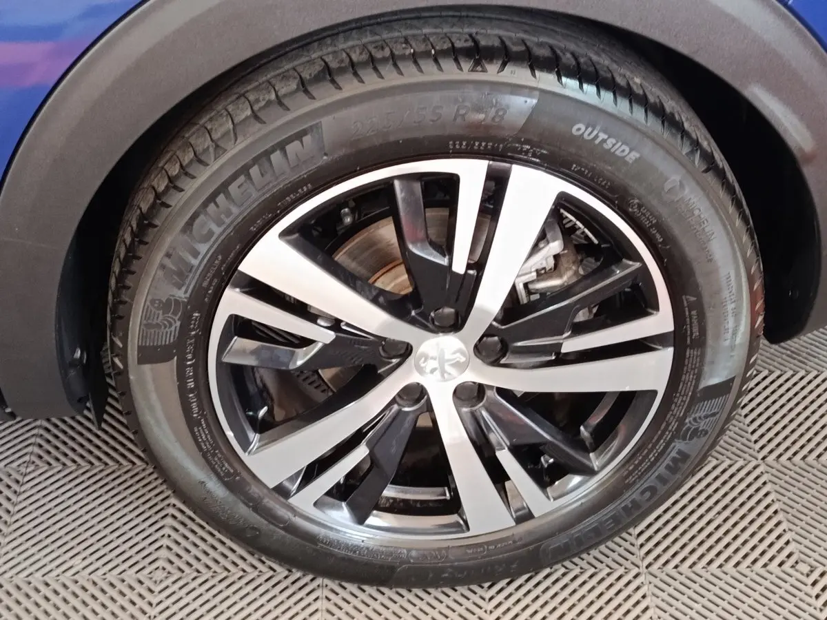 Gros plan sur la roue avant droite d’un Peugeot 3008 bleu, jante alliage bicolore et pneu Michelin visible.