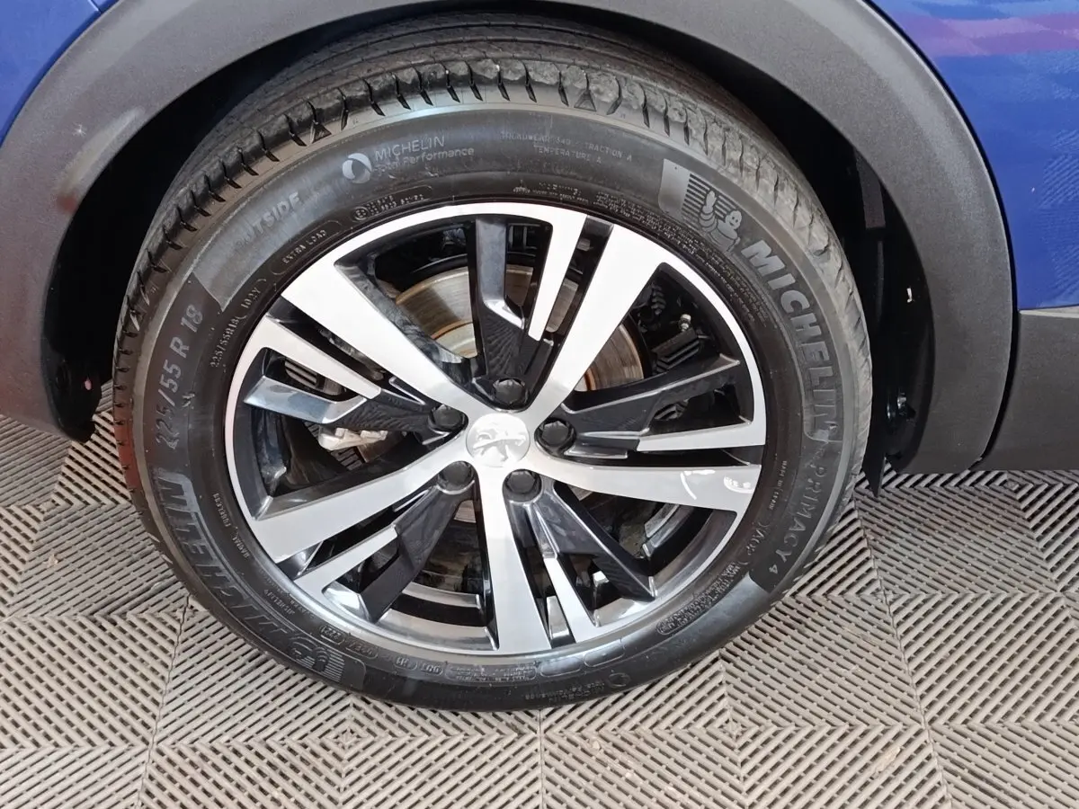 Gros plan sur la roue avant droite d’un Peugeot 3008 bleu, avec jante alliage bicolore et pneu Michelin.