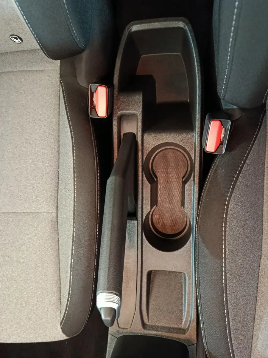 Vue plongeante sur la console centrale noire de la Renault Clio Evolution Blue dCi 100 avec frein à main et ceintures rouges.