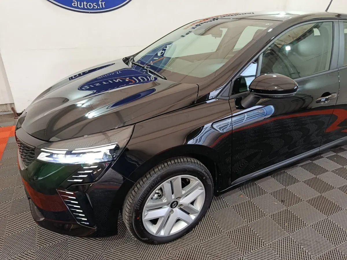 Vue 3/4 avant droit d'une Renault Clio noire 2025 avec phares LED allumés et jantes alliage argentées.