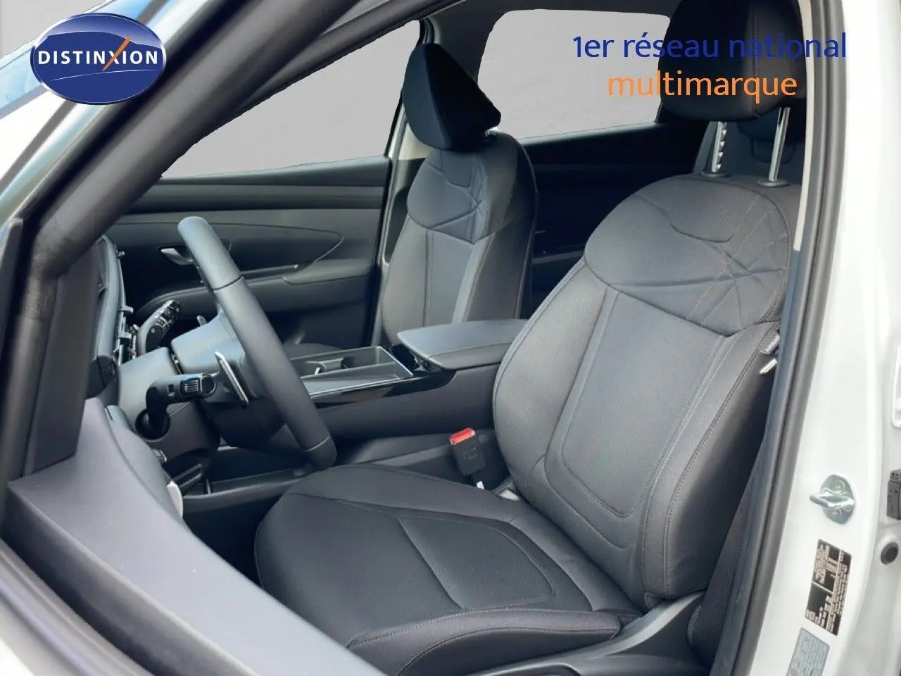 Vue intérieure côté conducteur du Hyundai Tucson blanc Atlas 2026, sièges tissu noir et volant multifonction.