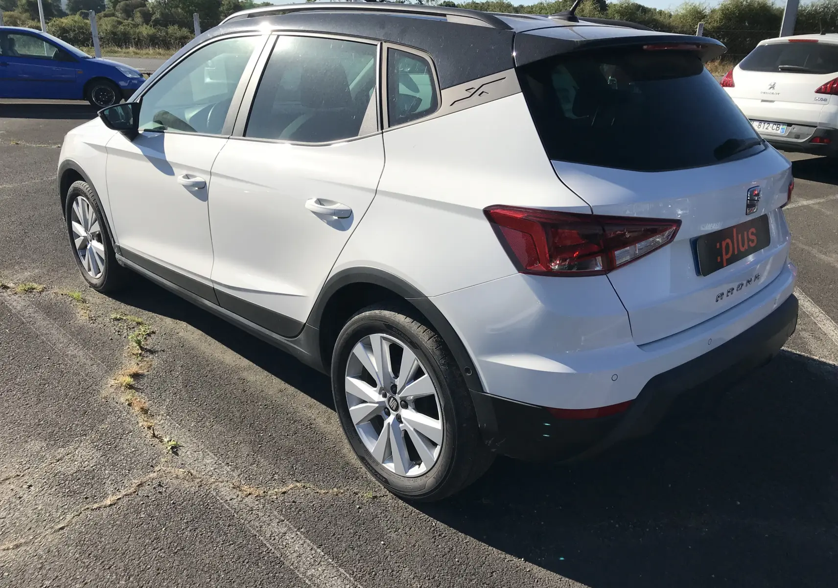 Vue 3/4 arrière droite d'un SEAT Arona blanc avec toit noir et jantes alliage sur parking ensoleillé.