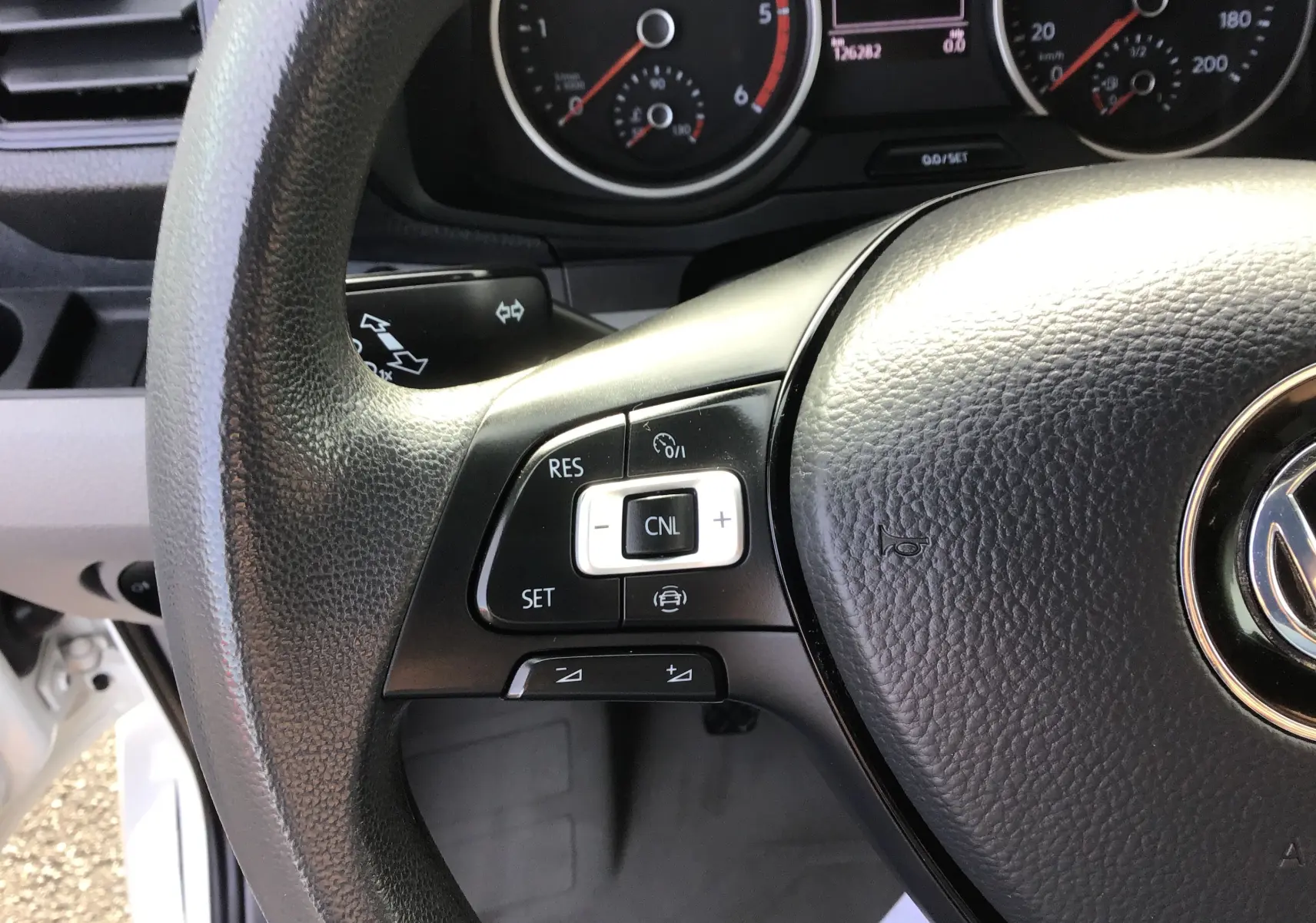 Gros plan sur le volant noir du Volkswagen Crafter blanc, montrant les commandes de régulateur de vitesse à gauche.