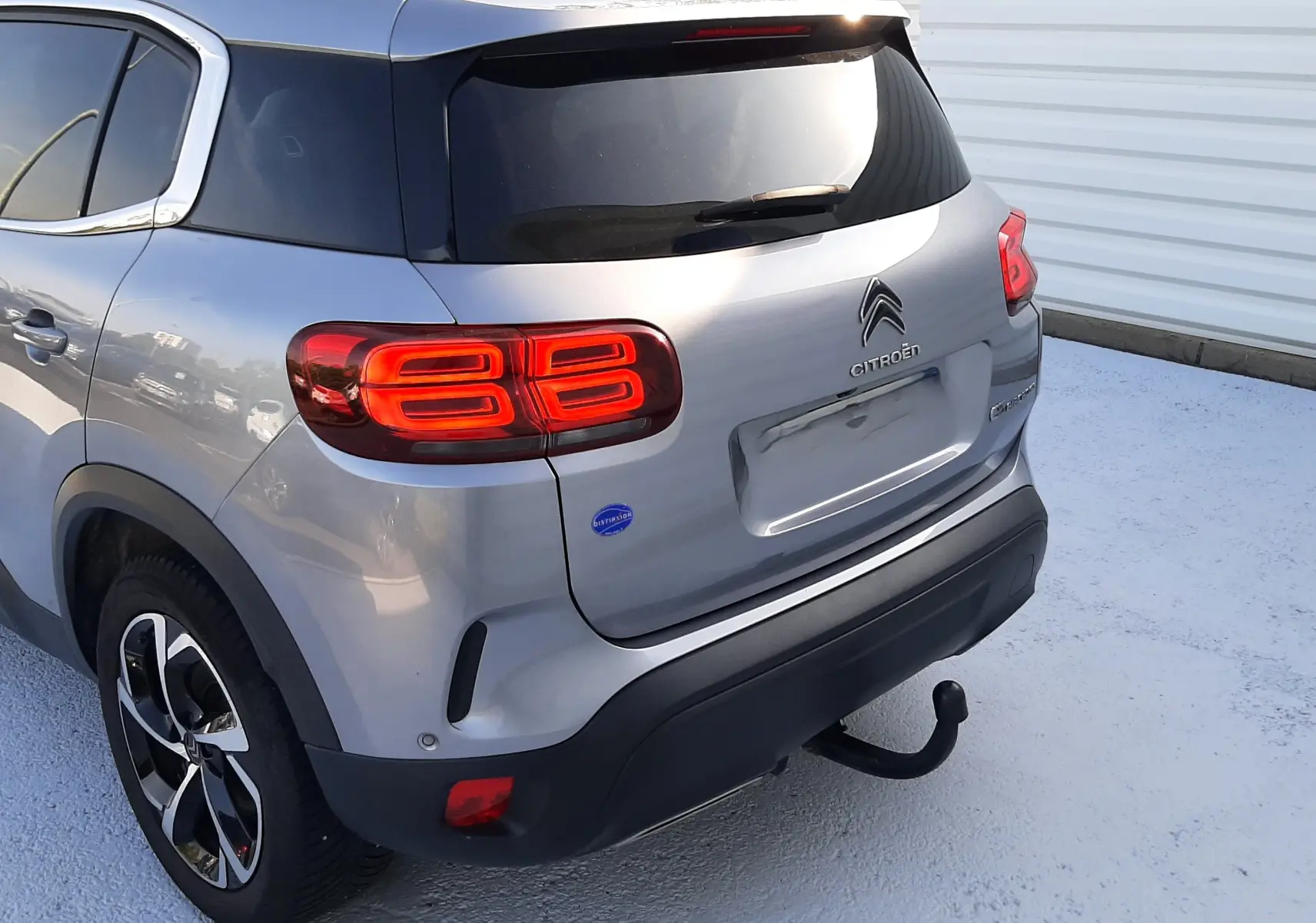 Vue 3/4 arrière droite d'un Citroën C5 Aircross gris Artense avec feux arrière allumés et attelage de remorque.