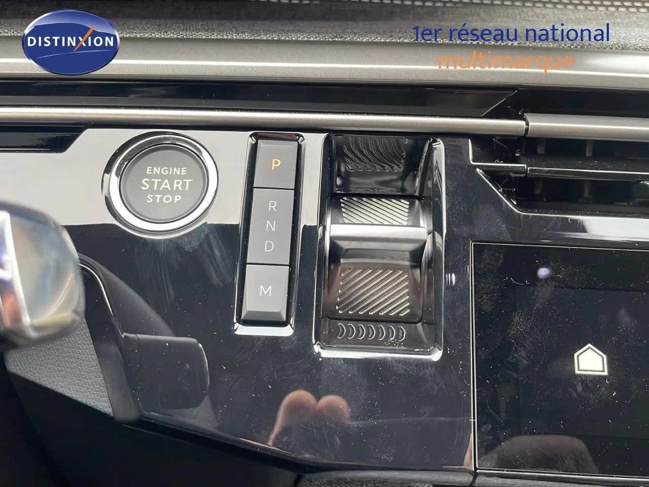 Gros plan sur la console centrale noire brillante du Peugeot 5008 Hybrid 2025 avec bouton start/stop et commandes de boîte auto.