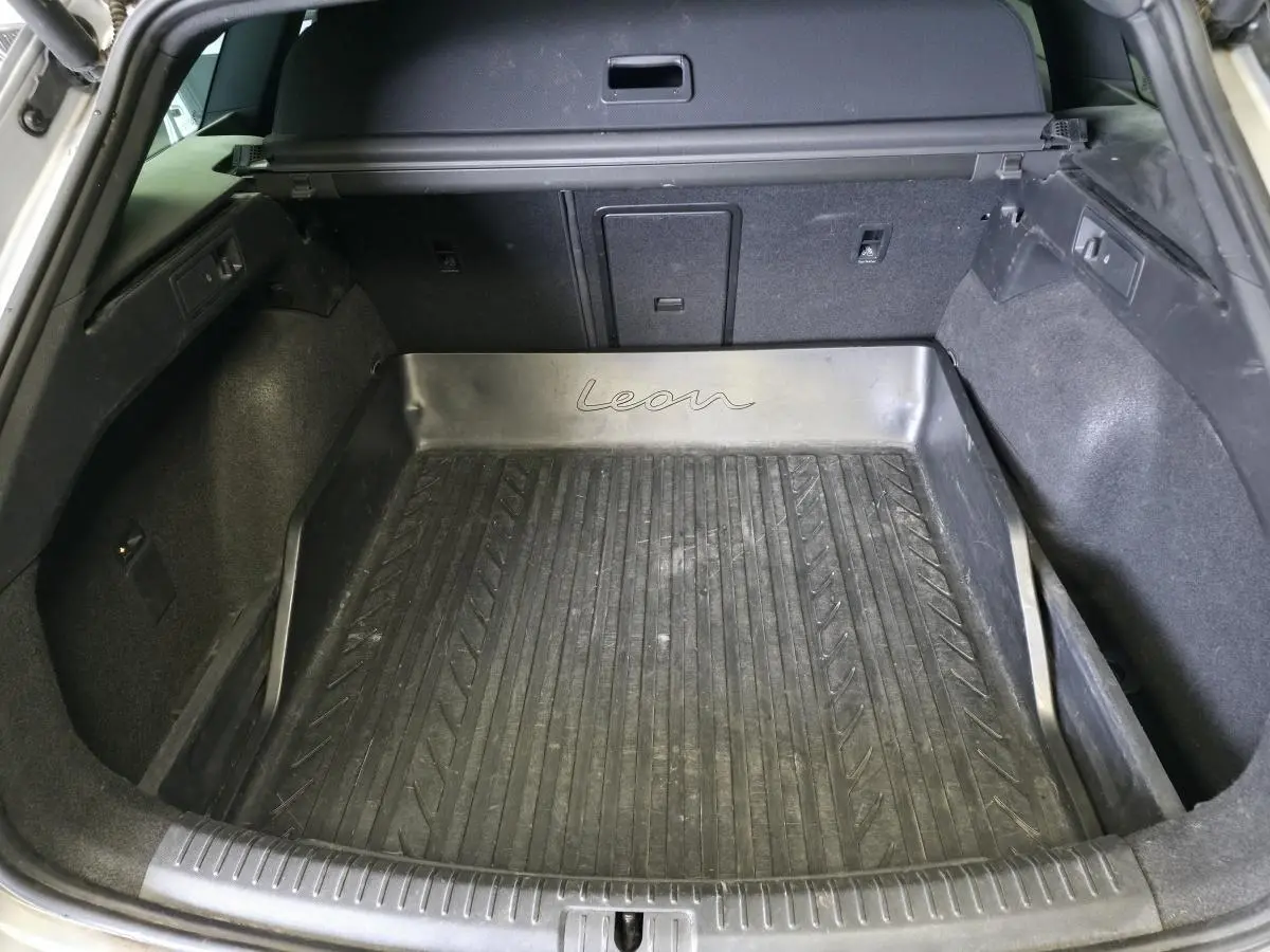 Vue intérieure du coffre spacieux d'un SEAT Leon Sportstourer gris avec tapis de coffre en caoutchouc marqué "Leon".