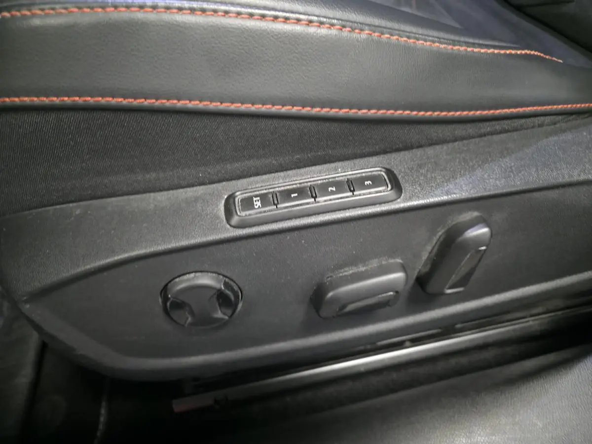 Détail des commandes de réglage électrique du siège conducteur noir avec surpiqûres rouges dans une SEAT Leon Sportstourer gris urbain.