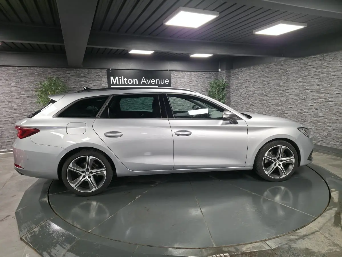 Vue de profil côté gauche d’un break SEAT Leon Sportstourer gris urbain avec jantes alliage et barres de toit chromées.