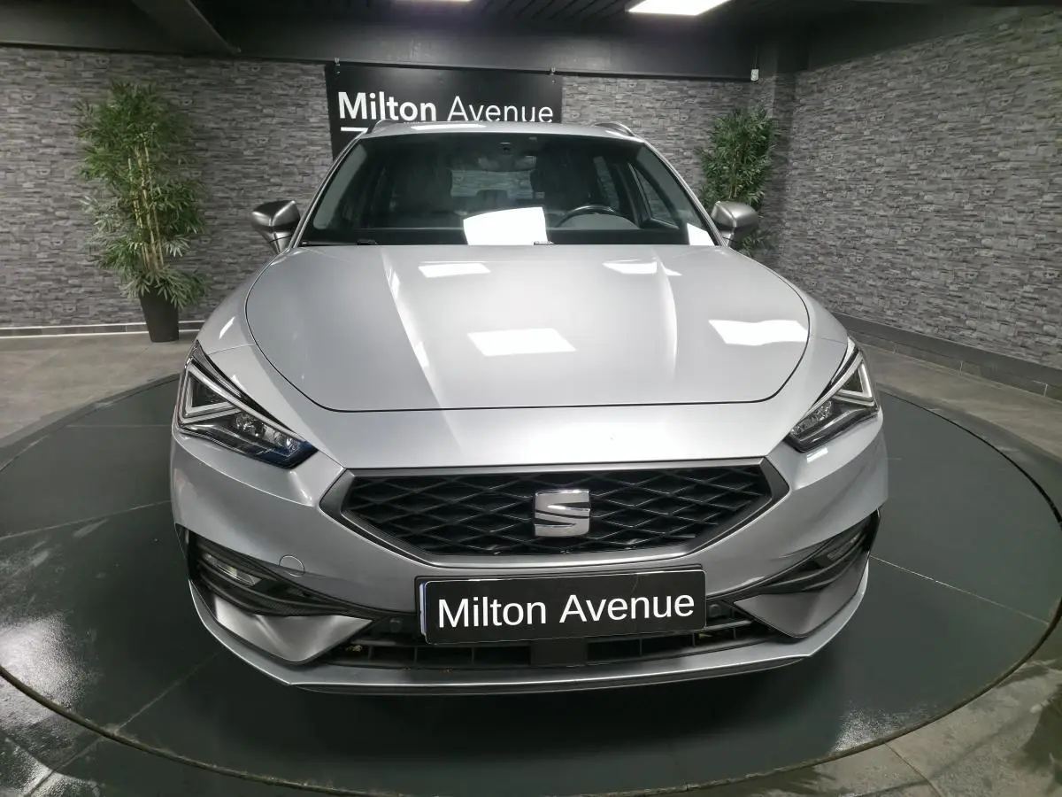 Vue avant d'une SEAT Leon Sportstourer gris urbain avec calandre noire et phares LED anguleux dans un showroom.