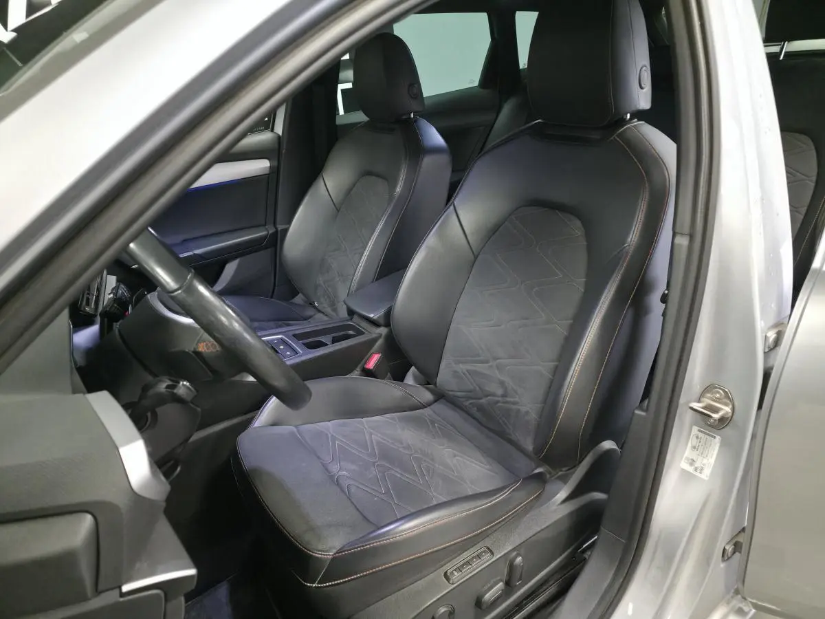 Vue intérieure côté conducteur d'une SEAT Leon Sportstourer gris urbain, sièges sport en suédine noire avec surpiqûres rouges.
