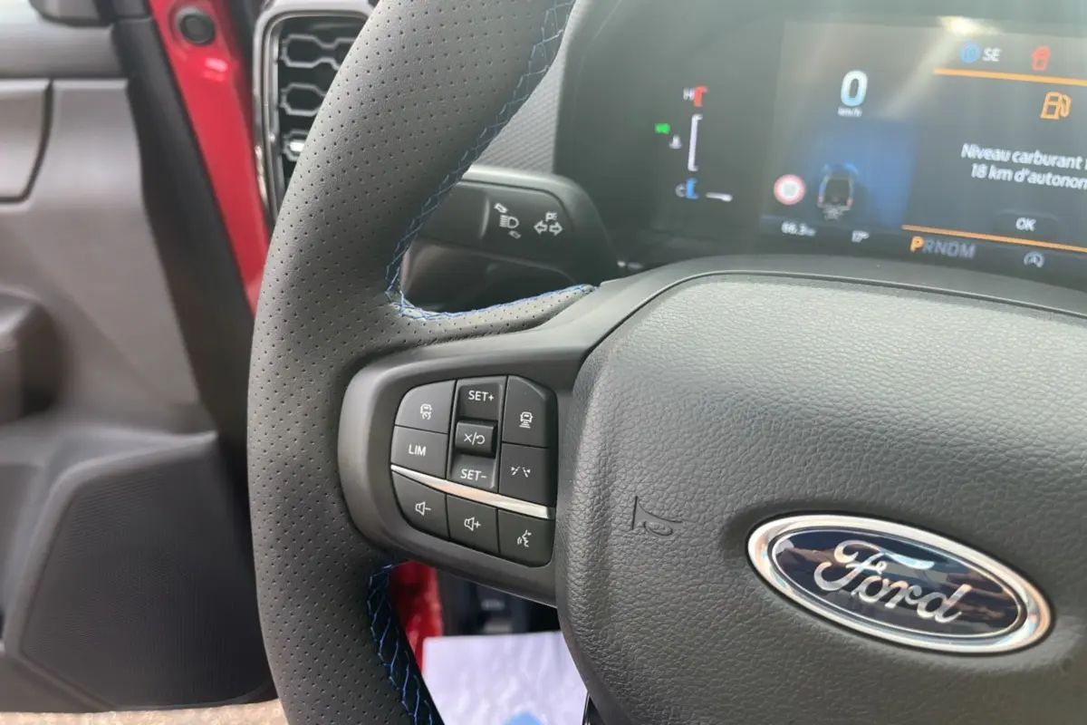 Vue rapprochée du volant cuir perforé avec surpiqûres bleues du Ford Ranger Lucid Red 2025, tableau de bord numérique visible.