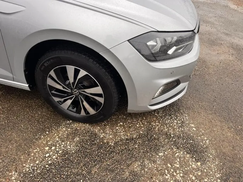 Gros plan sur l'avant droit gris Urano d'une Volkswagen Polo 2021, mettant en valeur le phare et la jante alu bicolore.