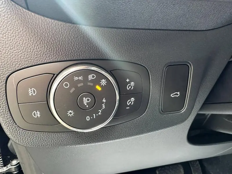 Gros plan sur le bouton de réglage des phares et l’ouverture du coffre dans l’habitacle d’un Ford Puma noir.