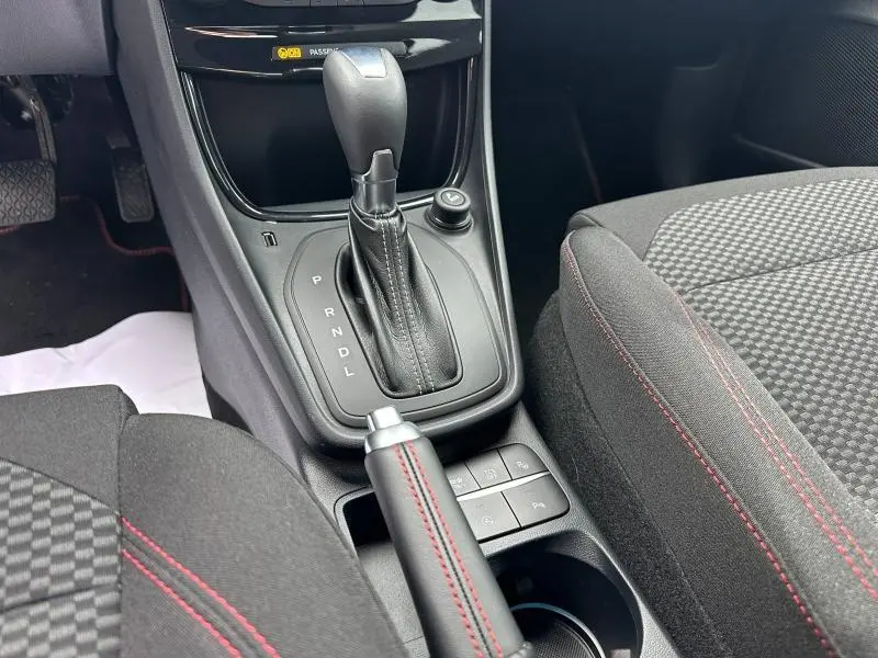 Gros plan sur la console centrale du Ford Puma 2024 noir, montrant levier de vitesse automatique et frein à main avec surpiqûres rouges.