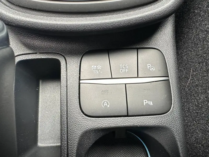 Gros plan sur les boutons de commande du système d’aide à la conduite dans un Ford Puma 2024 noir, intérieur en plastique texturé noir.