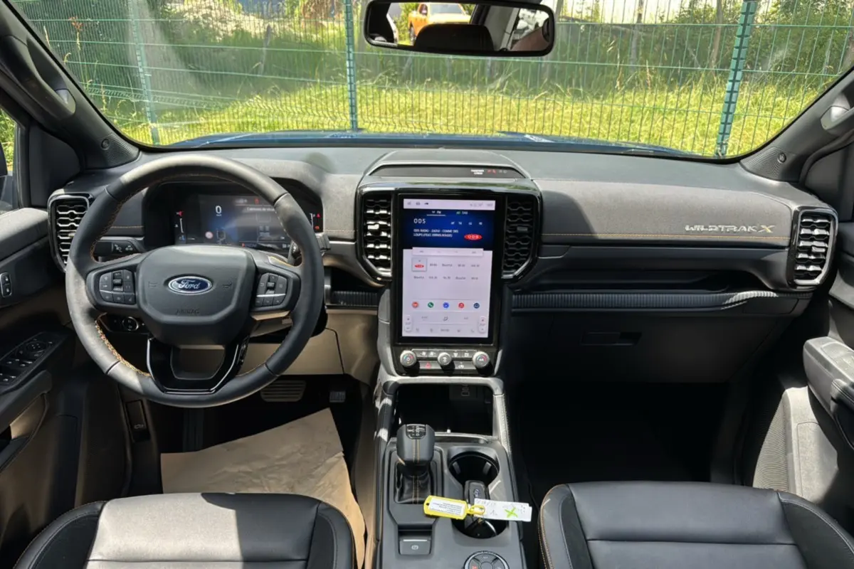 Vue intérieure avant du Ford Ranger Wildtrak X 2025, tableau de bord noir avec écran tactile vertical et volant multifonctions cuir.