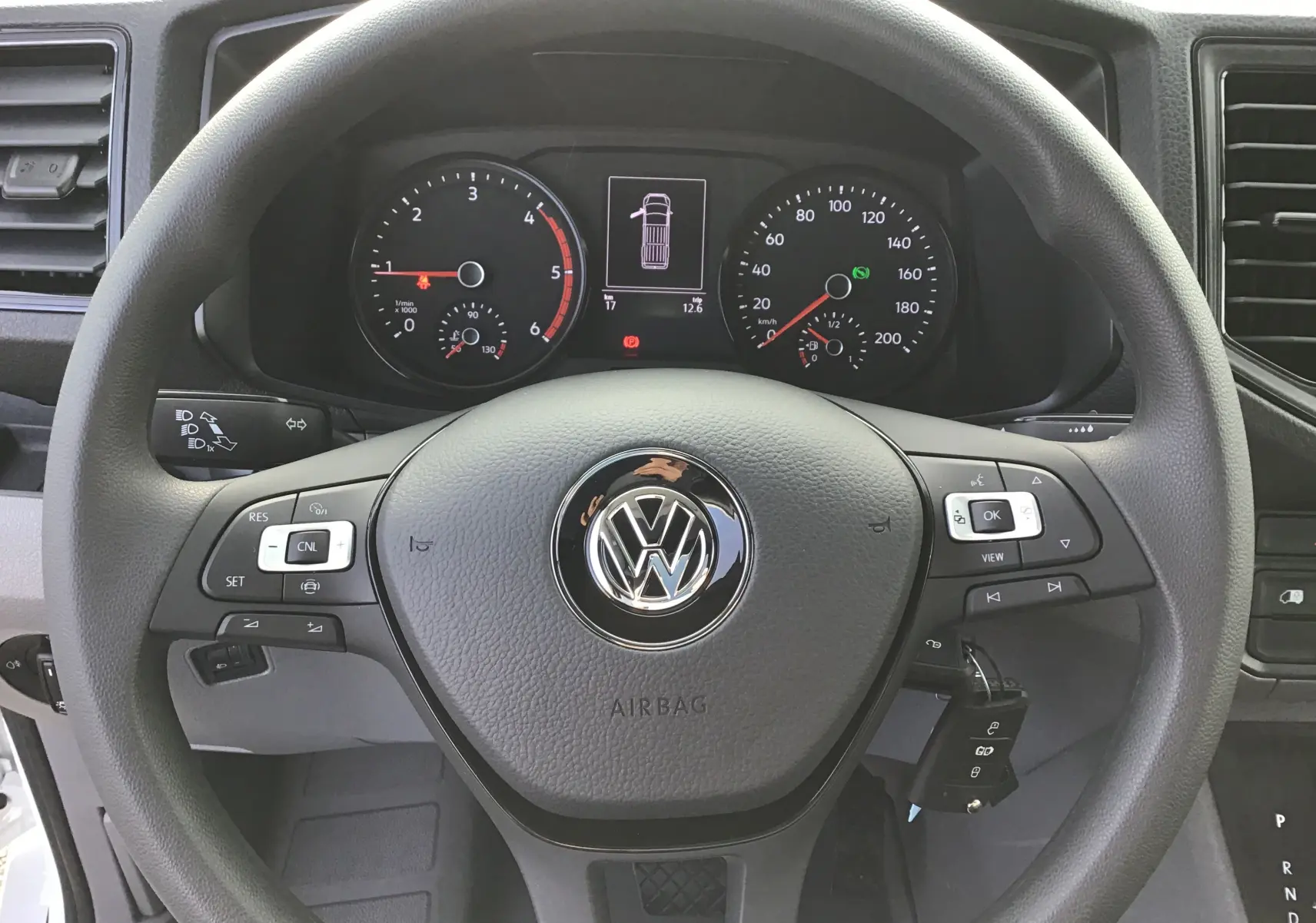 Vue rapprochée du volant noir et du tableau de bord du Volkswagen Crafter Fourgon blanc 2024 avec commandes au volant.