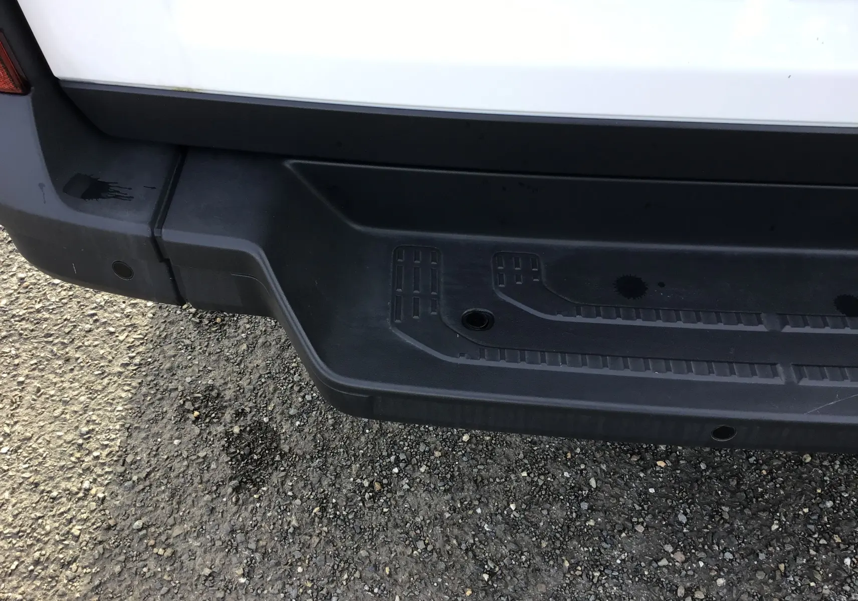 Gros plan sur le pare-chocs arrière noir du Volkswagen Crafter fourgon blanc, montrant la marche intégrée et capteurs de recul.